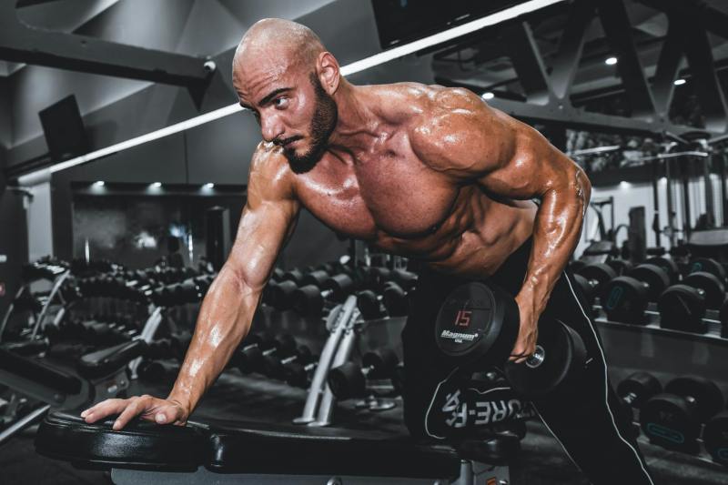 Man with shirt off in gym lifting one dumbbell