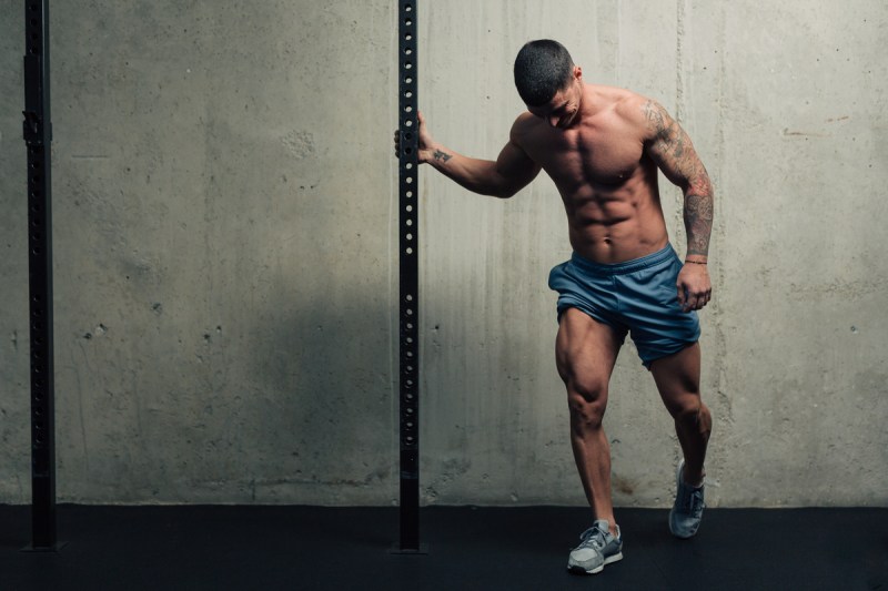 Young strong man posing and flexing his quadriceps legs muscles in a gym blue shorts holding